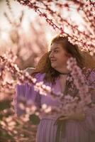 donna fioritura pesca frutteto. contro il fondale di un' pittoresco pesca frutteto, un' donna nel un' lungo rosa vestito e cappello gode un' tranquillo, calmo camminare nel il parco, circondato di il bellezza di natura. foto