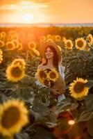 un' ragazza nel un' cappello su un' bellissimo campo di girasoli contro il cielo nel il sera leggero di un' estate tramonto. raggi di sole attraverso il fiore campo. naturale sfondo. foto