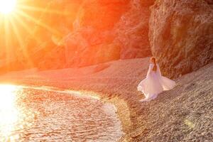 misterioso donna silhouette lungo capelli passeggiate su il spiaggia oceano acqua, mare ninfa vento ascolta per il onda. lanci su un' lungo bianca vestire, un' divine tramonto. artistico foto a partire dal il indietro senza un' viso