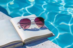 paio di occhiali da sole riposo su libro di il bordo piscina, esemplificativo pigro estate giorni foto