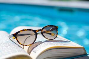 paio di occhiali da sole riposo su libro di il bordo piscina, esemplificativo pigro estate giorni foto