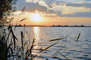 tramonto al di sopra di tranquillo lago, getto caldo splendore al di sopra di il acqua e circostante paesaggio foto