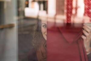 allegro donna con Riccio capelli sbirciando attraverso un' bicchiere finestra nel un' vivace urbano ambiente foto