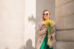 donna Tenere giallo tulipani, pendente contro pietra parete. Da donna vacanza concetto, dando fiori. foto