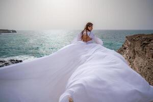 contento la libertà donna su il spiaggia godendo e in posa nel bianca vestire. posteriore Visualizza di un' ragazza nel un' svolazzanti bianca vestito nel il vento. vacanze, vacanze a mare. foto