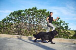 pieno lunghezza ritratto di giovane attivo donna in esecuzione e a piedi sua cane su guinzaglio su il natura all'aperto. le persone. giocando animali domestici. sport. attivo e salutare stile di vita concetto foto