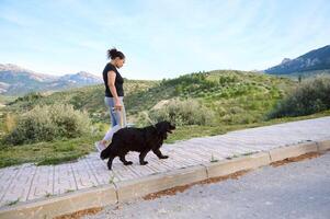 pieno lunghezza tiro di un' donna nel attivo indossare, a piedi sua cane su il montagne natura. domestico animali, animali domestici e persone concetto foto