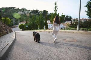 pieno lunghezza ritratto di un' carino poco bambino ragazza nel abbigliamento sportivo, a piedi sua cane su guinzaglio su il strada. persone e animali. giocando animali domestici concetto foto