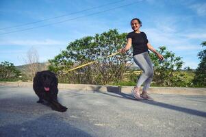 donna a piedi sua cane su guinzaglio nel il natura su un' bellissimo soleggiato estate giorno. bella femmina atleta in esecuzione con sua animale domestico nel il mattina. giocando animali domestici concetto foto