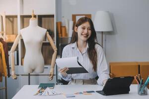 ritratto bellissimo Sorridi asiatico progettista donna uso computer nel sarto tessuto moda piccolo attività commerciale in linea officina. giovane proprietario avviare imprenditore. creativo ragazza tessile indumento pmi attività commerciale concetto foto