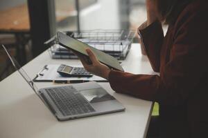 tiro di un' asiatico giovane attività commerciale femmina Lavorando su il computer portatile nel sua postazione di lavoro. foto