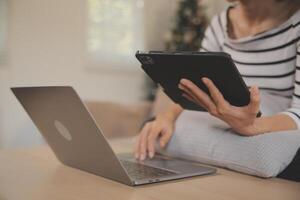 giovane attraente asiatico donna riposo utilizzando navigazione tavoletta computer su divano a casa, contento ragazza seduta su divano rilassare lettura digitale aggeggio con emozionato, comunicazione e stile di vita concetto. foto