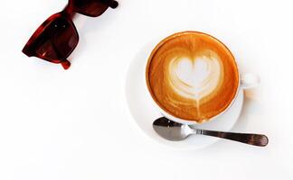 superiore su o piatto posare di tazza di caldo arte latte macchiato caffè o cappuccino caffè e Marrone occhiali da sole isolato su bianca sfondo con copia spazio. rinfresco potabile a bar negozio nel il mattina. foto