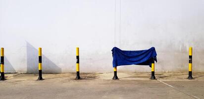 blu brandelli, cotone, tappeto o tessuto sospeso su piccolo giallo e nero Torre con grigio parete sfondo. foto