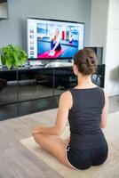 giovane donna è fare fitness a casa nel vivente camera mentre Guardando e partecipando nel un' classe foto
