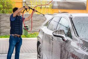 giovane uomo lavaggi il suo auto a un' Fai da te auto lavare utilizzando un' tubo flessibile con pressurizzato acqua e schiuma. foto