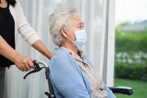 aiuta la donna anziana asiatica anziana o anziana seduta su una sedia a rotelle e indossa una maschera facciale per proteggere l'infezione di sicurezza covid-19 coronavirus. foto
