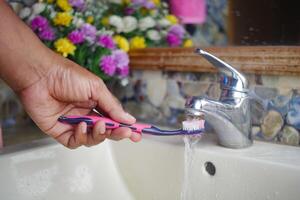 lento movimento di Tenere spazzolino sotto fluente acqua nel bagno, avvicinamento. foto