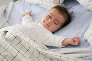 bambina sorridente sdraiata su un letto che dorme su lenzuola blu foto