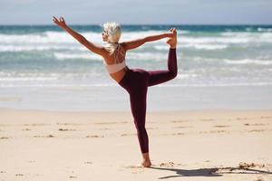 donna bionda caucasica che pratica yoga in spiaggia foto