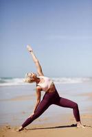donna bionda caucasica che pratica yoga in spiaggia foto