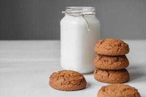 latte in un barattolo di vetro e biscotti di farina d'avena su un tavolo bianco foto
