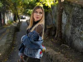 bella bionda con i capelli fluenti in una giacca di jeans si trova per strada sullo sfondo di una scala di pietra foto