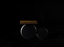 pettine di legno e barattoli di cera per barba e baffi su sfondo nero foto