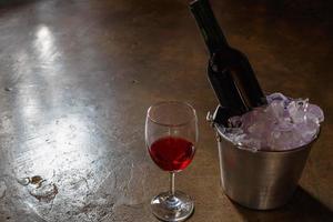 bottiglia di vino rosso in un secchiello del ghiaccio e un bicchiere di vino rosso foto