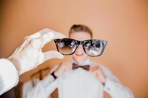 occhiali da sole in mano sullo sfondo di un giovane ragazzo in camicia e cravatta foto