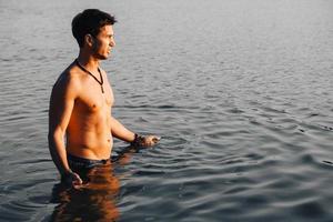 uomo con muscoli perfetti sta nell'acqua al tramonto foto