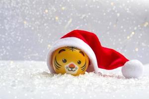 il simbolo del nuovo anno è una tigre con un cappello da Babbo Natale sulla neve su uno sfondo di luci bokeh. primo piano del nuovo anno