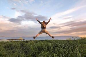 uomo escursionista nel Camo pantaloncini e zaino su superiore di verde collina, mani su, Visualizza su selvaggio atlantico modo a Galway, Irlanda, libertà, avventura e stile di vita concetto, natura sfondo foto