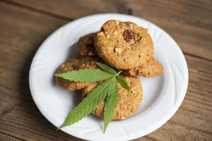 biscotti al cioccolato con foglia di cannabis - pianta di foglie di marijuana su piatto bianco sul tavolo di legno erba naturale, concetto di cibo di cannabis foto