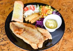 filetto di pesce fritto - piatto di pesce bistecca di pesce con salsa crema patatine fritte pane e verdure fresche sul piatto