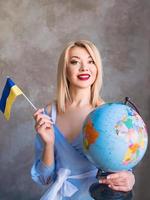 bella donna slava bionda allegra attraente che tiene globo e bandiera ucraina. foto