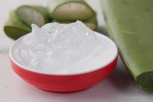 aloe vera fresca affettata e gel liquido in contenitore di plastica su sfondo bianco foto