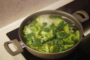 cucinando broccoli nel padella su elettrico stufa foto