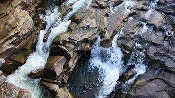 vista dall'alto verso il basso della cascata. vista dall'alto del torrente, l'acqua scorre sulle pietre. cascata di montagna rocciosa. paesaggio aereo montagna cascata rocciosa fiume ruscello sfondo scenico naturale immagine foto