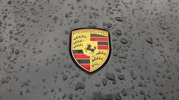 ucraina, kiev - 27 marzo 2020. logo porsche primo piano su un'auto nera con gocce di pioggia. emblema del cofano di un'auto sportiva. copia spazio, fotografia editoriale. mostra automobilistica tedesca sulla strada. foto