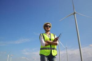 il fiducioso donna nel bianca casco Lavorando con digitale tavoletta e utilizzando walkie talkie a un' rinnovabile energia azienda agricola. femmina ispettore controllo il funzionamento di vento turbine all'aperto foto