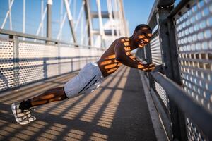 giovane afroamericano uomo è esercizio su il ponte nel il città. lui è fare sollevamento. foto