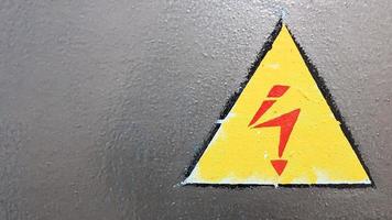 segnale di sicurezza giallo e rosso su fondo in metallo argentato. fulmini ad alta tensione in un triangolo attenzione attenzione pericolo elettricità morte. foto