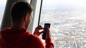 un giovane fa una foto del paesaggio urbano su uno smartphone. concetto di turismo. un uomo fotografa una città da un ponte di osservazione attraverso un vetro dall'alto.