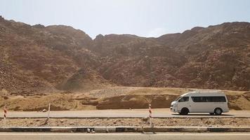 Egitto, Dahab - 17 ottobre 2019. un minibus commerciale bianco per passeggeri viaggia con i turisti su una strada asfaltata nel deserto sullo sfondo di bellissime montagne rocciose. foto