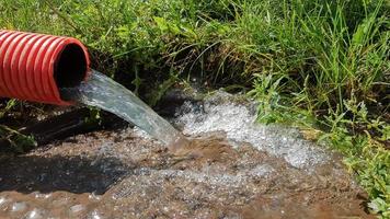 pompare acqua dalla zona alluvionale. sistema fognario. acque reflue industriali. scarichi fognari da un tubo di fognatura rosso corrugato in plastica in un tombino fognario in città foto