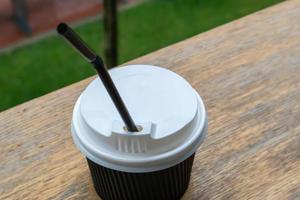 una tazza da caffè di carta nera con coperchio all'aperto in estate con tempo soleggiato su un tavolo di legno di un bar, una caffetteria o un ristorante. foto