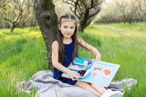 un' bambino ragazza è lettura un' libro nel il parco foto