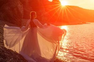 misterioso donna silhouette lungo capelli passeggiate su il spiaggia oceano acqua, mare ninfa vento ascolta per il onda. lanci su un' lungo bianca vestire, un' divine tramonto. artistico foto a partire dal il indietro senza un' viso