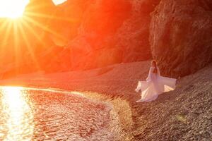 misterioso donna silhouette lungo capelli passeggiate su il spiaggia oceano acqua, mare ninfa vento ascolta per il onda. lanci su un' lungo bianca vestire, un' divine tramonto. artistico foto a partire dal il indietro senza un' viso